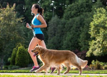Woman jogging with her dog along a leafy path, reflecting an active lifestyle and wellbeing focus.